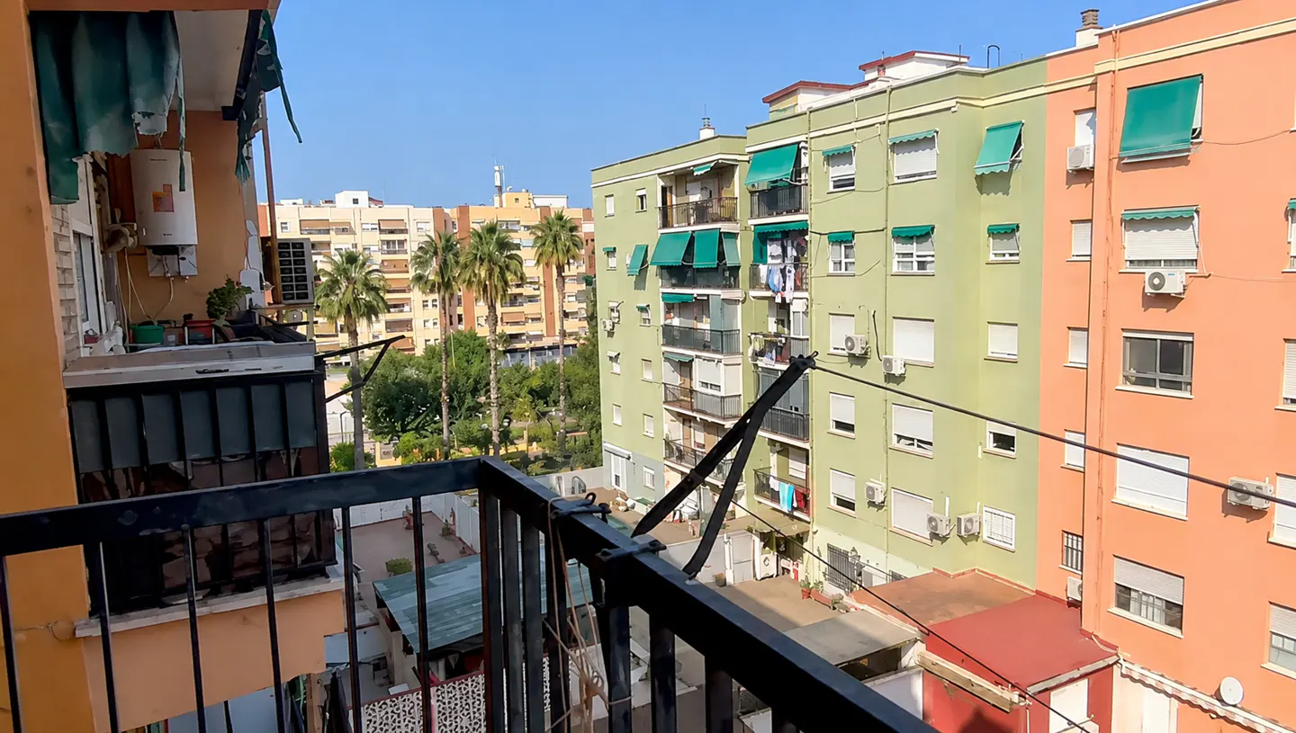 View from a balcony with black railings overlooking colorful apartment buildings and palm trees on a sunny day.