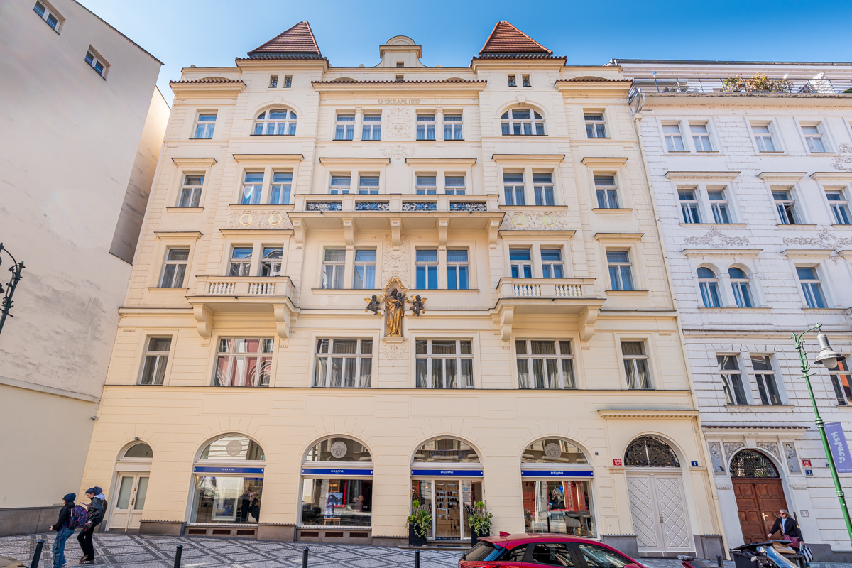 A cream-colored historic building with a golden statue on the facade, arched storefronts, and a cobblestone street. [AI-generated text]