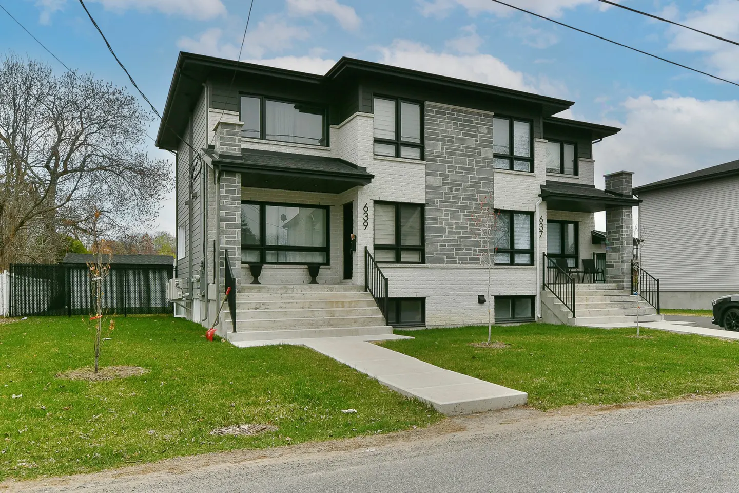 A two-story duplex with a gray stone and white brick facade, black trim, and concrete steps leading to each entrance.