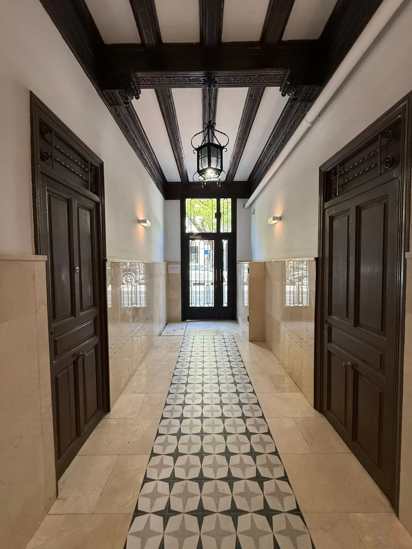 Hallway with dark wood beams, a patterned tile floor, and two dark wood doors on either side. A black lantern hangs from the ceiling.