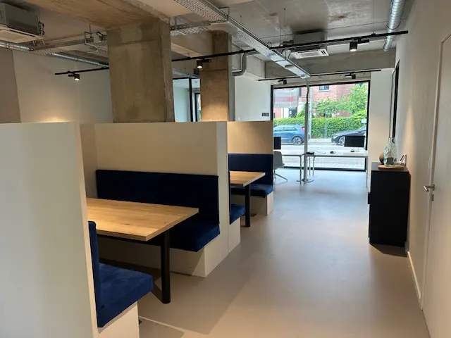 Interior view of a modern office space with booth seating, wood tables, and large windows.