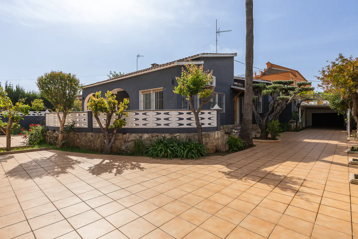 Exterior of a gray single-story house with a tiled driveway and a white patterned fence.