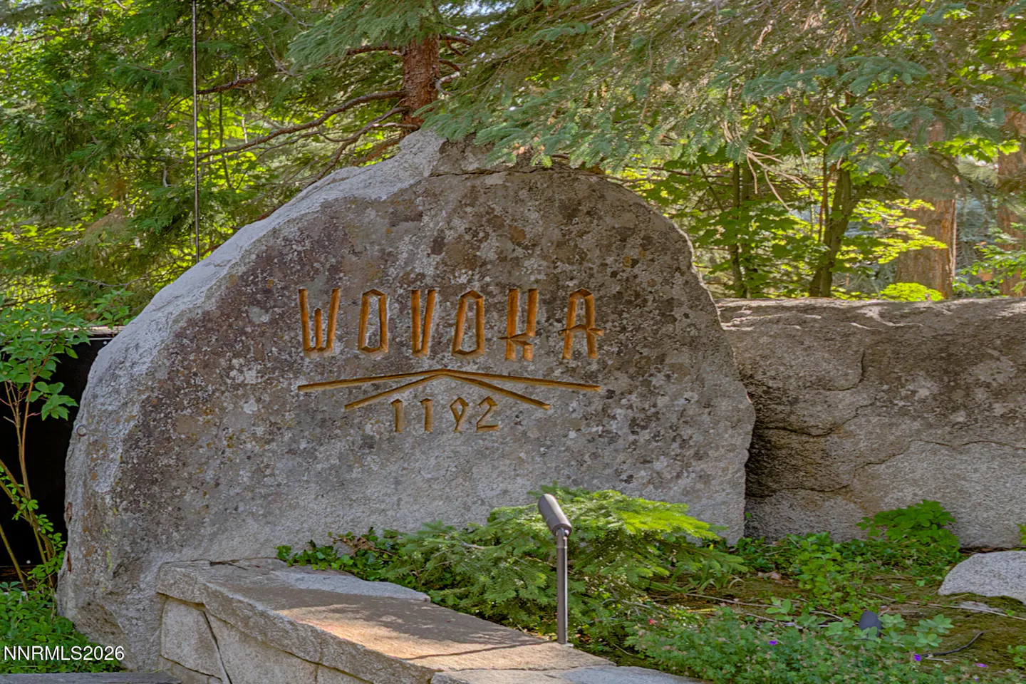 Large gray stone with "WOVOHA 1192" carved into it, surrounded by green foliage and trees.