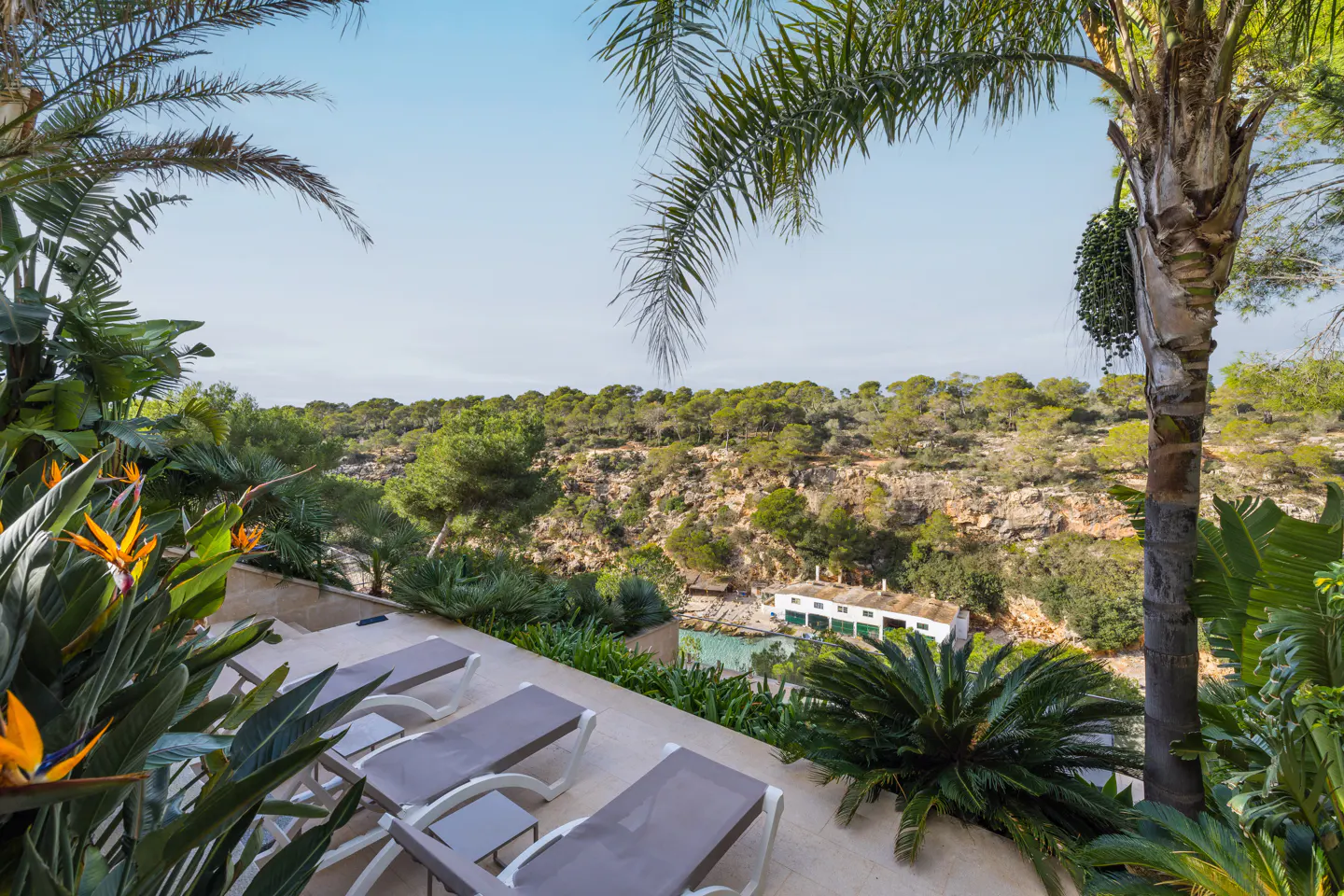 Outdoor patio with three lounge chairs overlooking a lush green landscape and a building near the water.