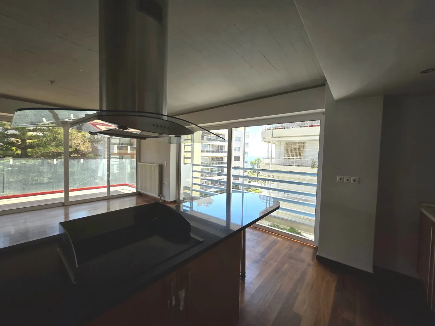 A modern kitchen with a black countertop island and stainless steel range hood. Large windows offer a view of the city and ocean. Hardwood floors add warmth.