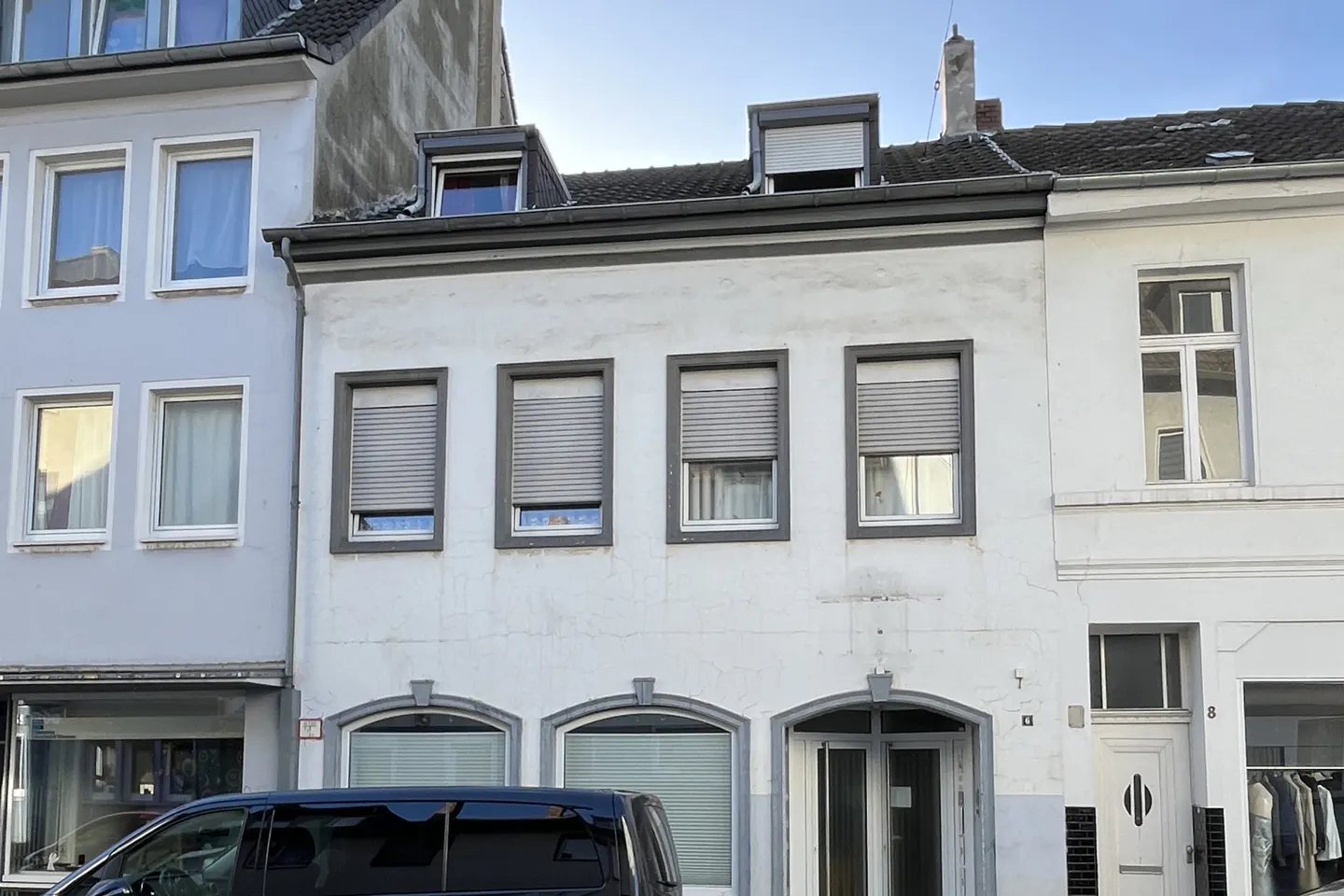 Exterior of a white, two-story building with gray trim and window shutters. A black van is parked in front.