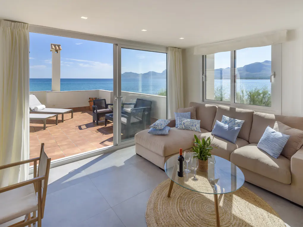 Living room with beige sectional sofa, blue pillows, glass table, and balcony with ocean view.
