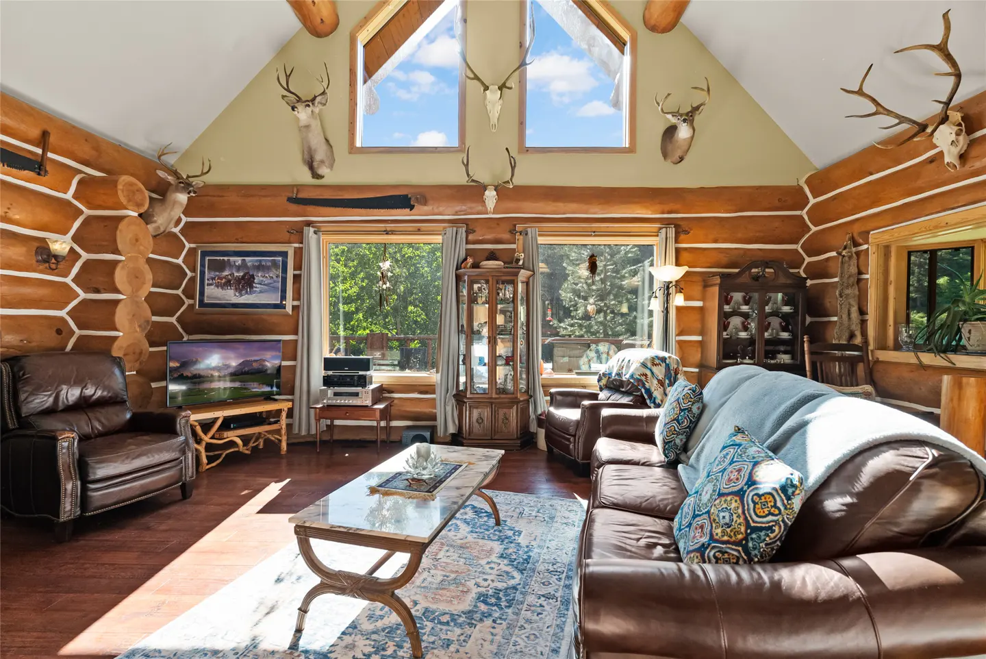 Living room in a log cabin with leather furniture, a marble coffee table, and mounted deer heads.