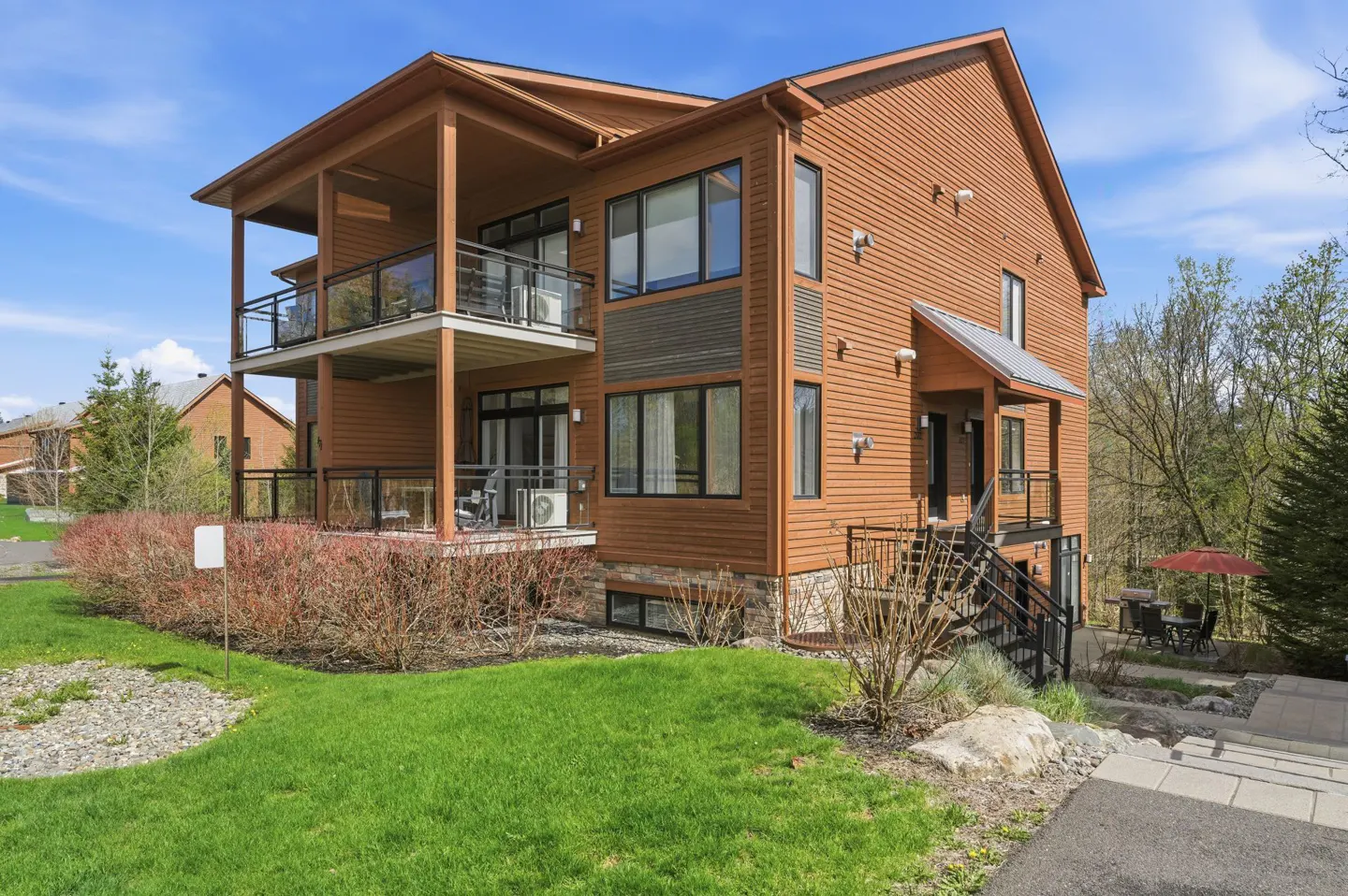 A two-story brown house with balconies, black framed windows, and a green lawn.