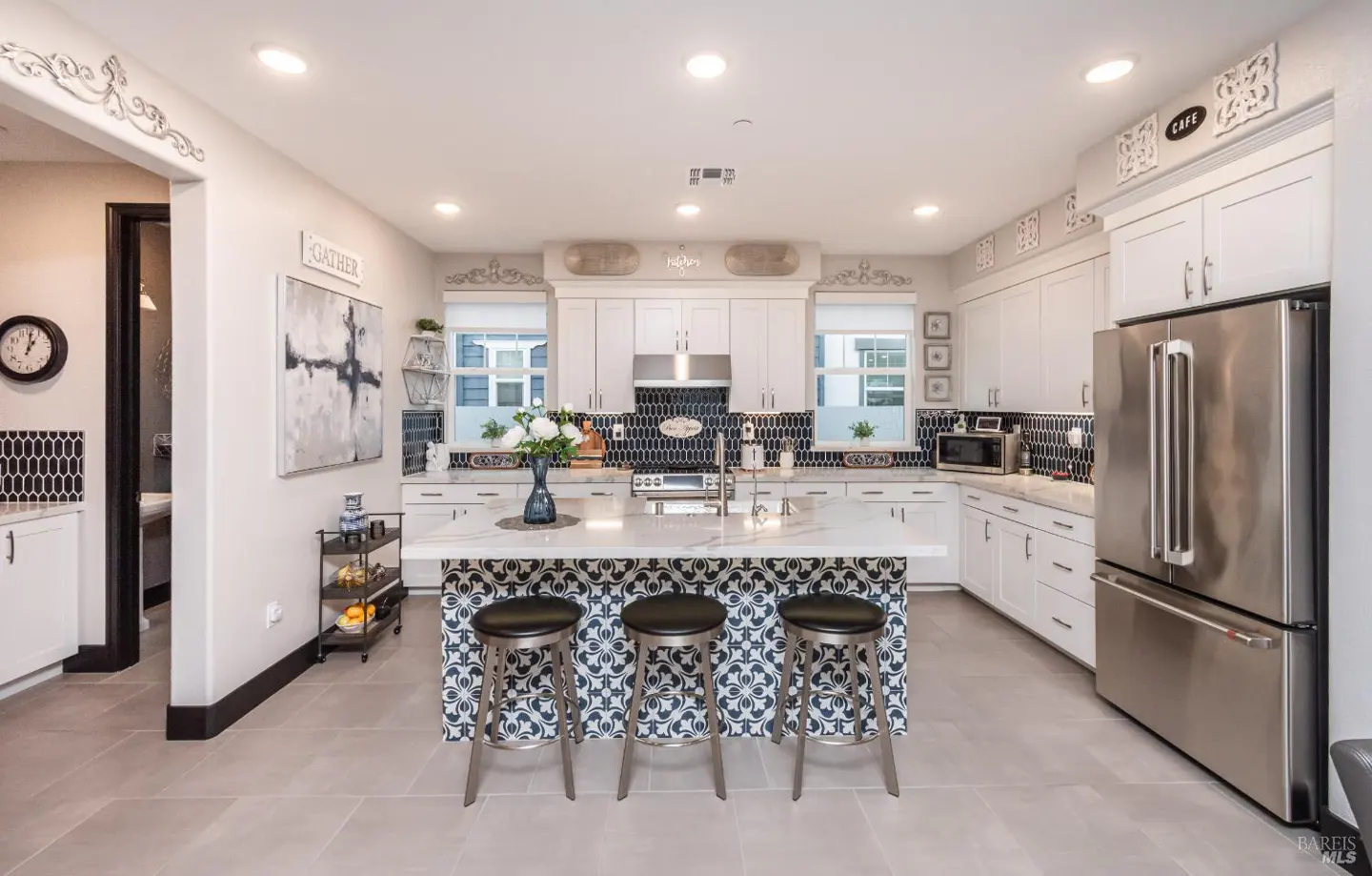 Bright kitchen with white cabinets, stainless steel appliances, and a patterned island with three stools.