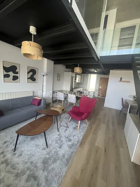 Modern loft living room with a grey sofa, red armchair, wooden coffee tables, and a mezzanine level with black ceilings.