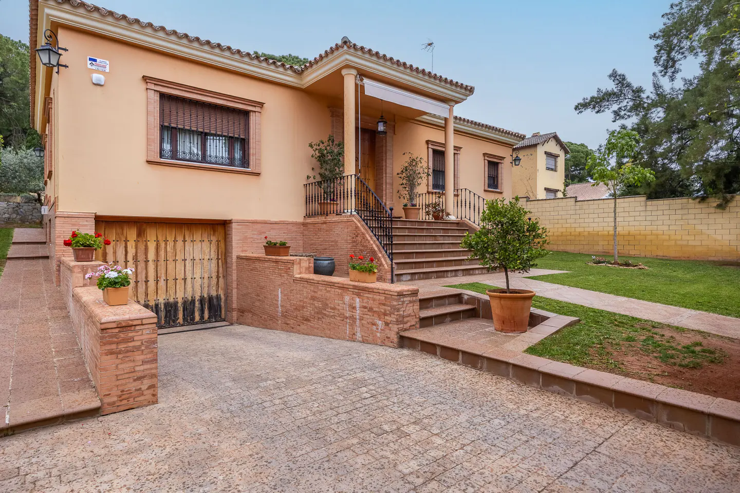 Exterior view of a peach-colored, single-story house with a tile roof, a garage, and a landscaped yard.