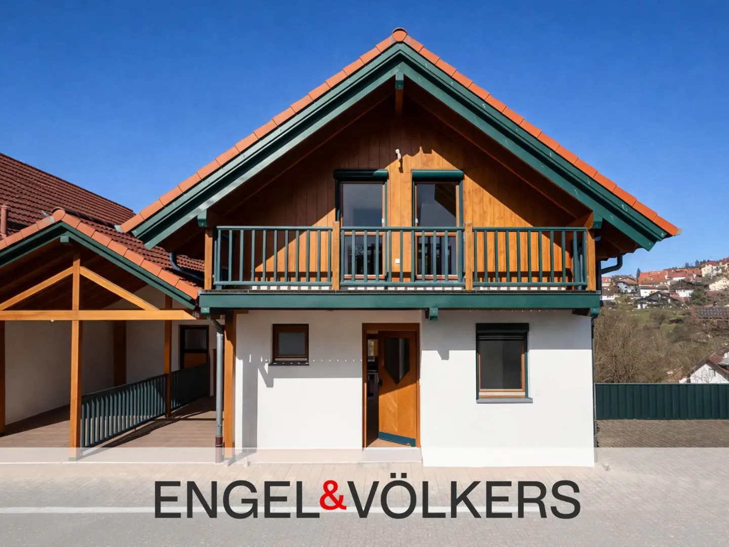 Two-story house with a balcony, white walls, and a red-tiled roof. The trim is green, and the door is open. The sky is blue.