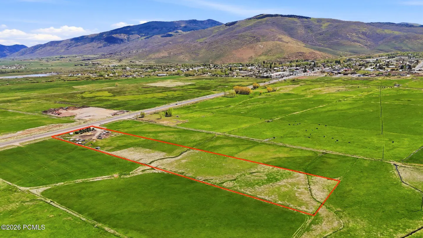 Aerial view of a green field outlined in red, with mountains and a town in the background.