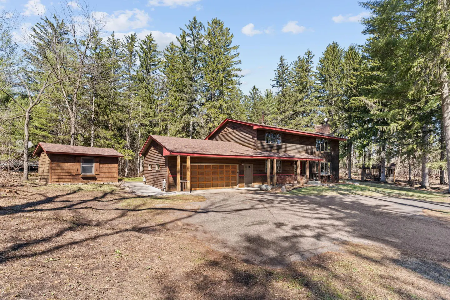 Two-story brown house with a brown roof and garage, surrounded by tall green trees and a blue sky.