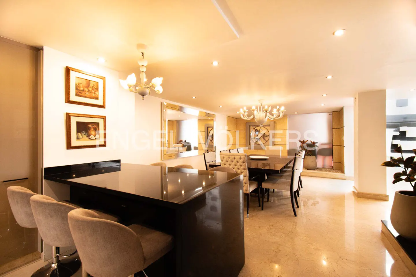Open-concept dining area with a black island, beige chairs, and a dark wood table under a chandelier.