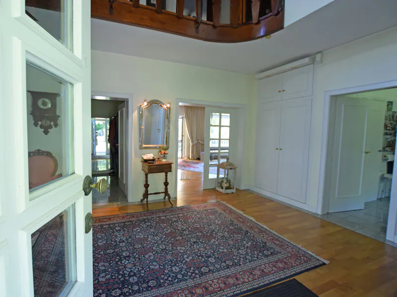 Open white front door reveals a foyer with a large rug, wood floors, and a wooden staircase above.
