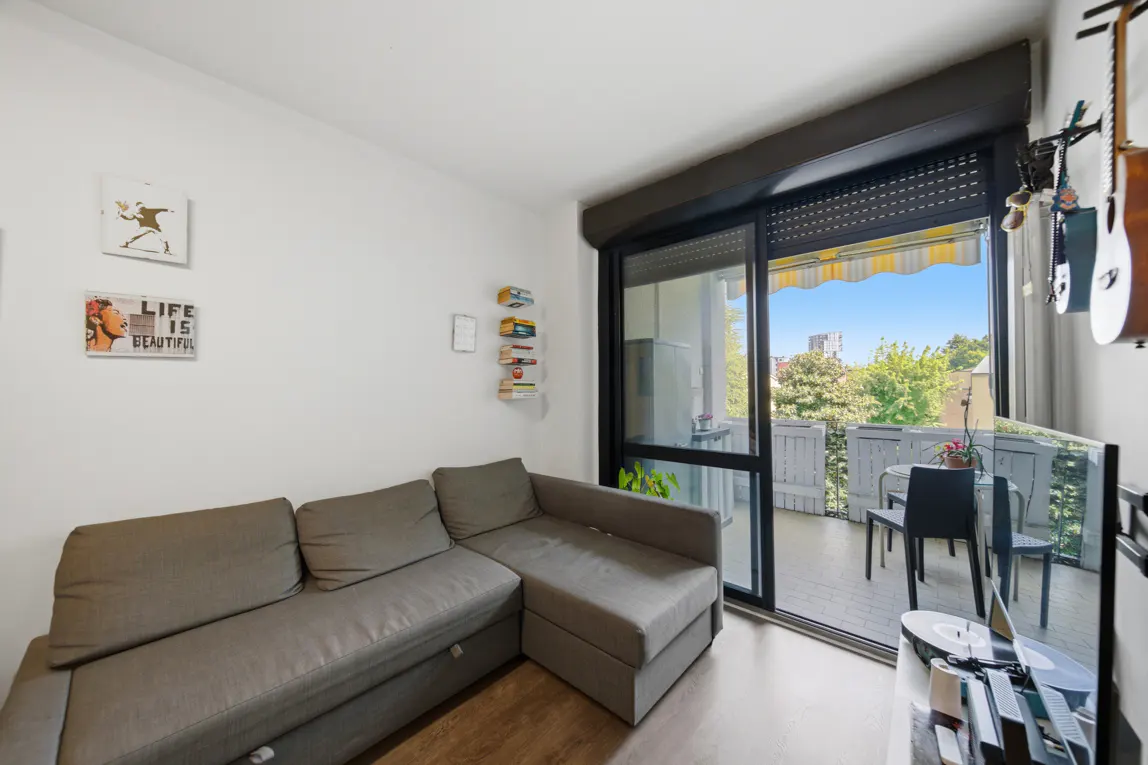 Living room with gray sectional sofa, white walls with art, and sliding glass doors to a balcony with table and chairs.