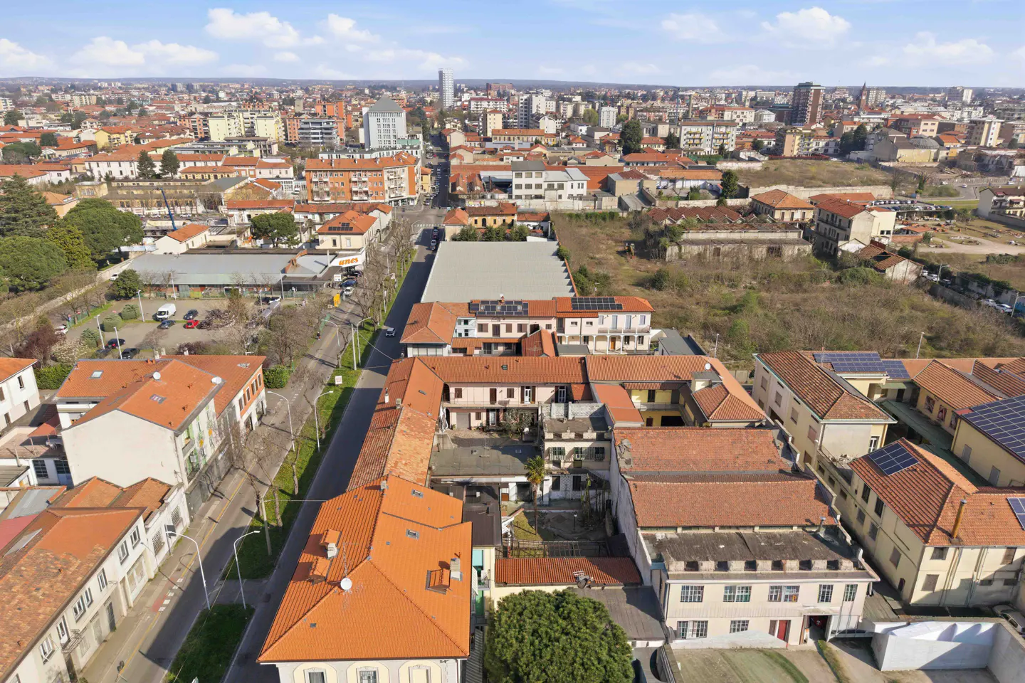 Aerial view of a European city with red-tiled roofs, buildings, and a street running through the center.