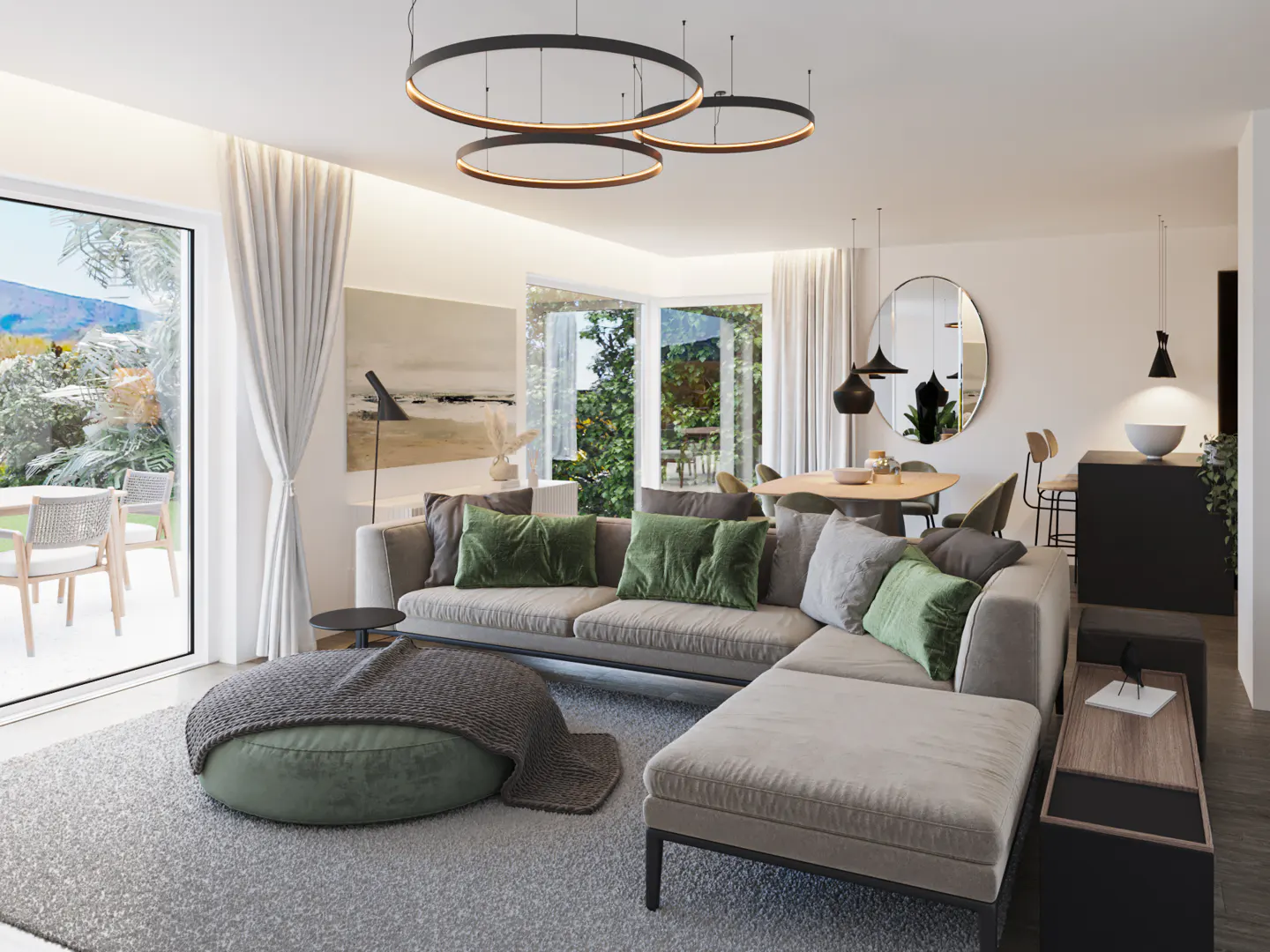 Bright living room with a gray sectional sofa, green pillows, and a round ottoman. Circular pendant lights hang above, and a dining area is visible in the background.