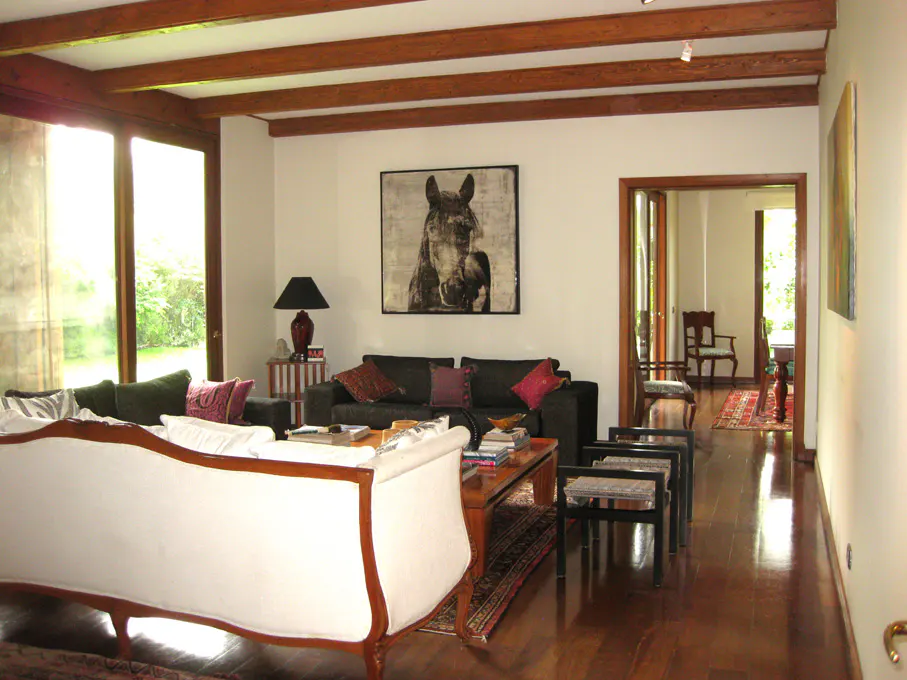 A living room with hardwood floors, exposed beams, and a horse painting. There are sofas, chairs, and a coffee table.