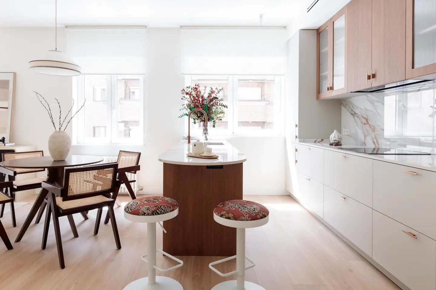 Bright, modern kitchen with white cabinets, wood accents, and a marble backsplash. A round dining table and two bar stools are visible.