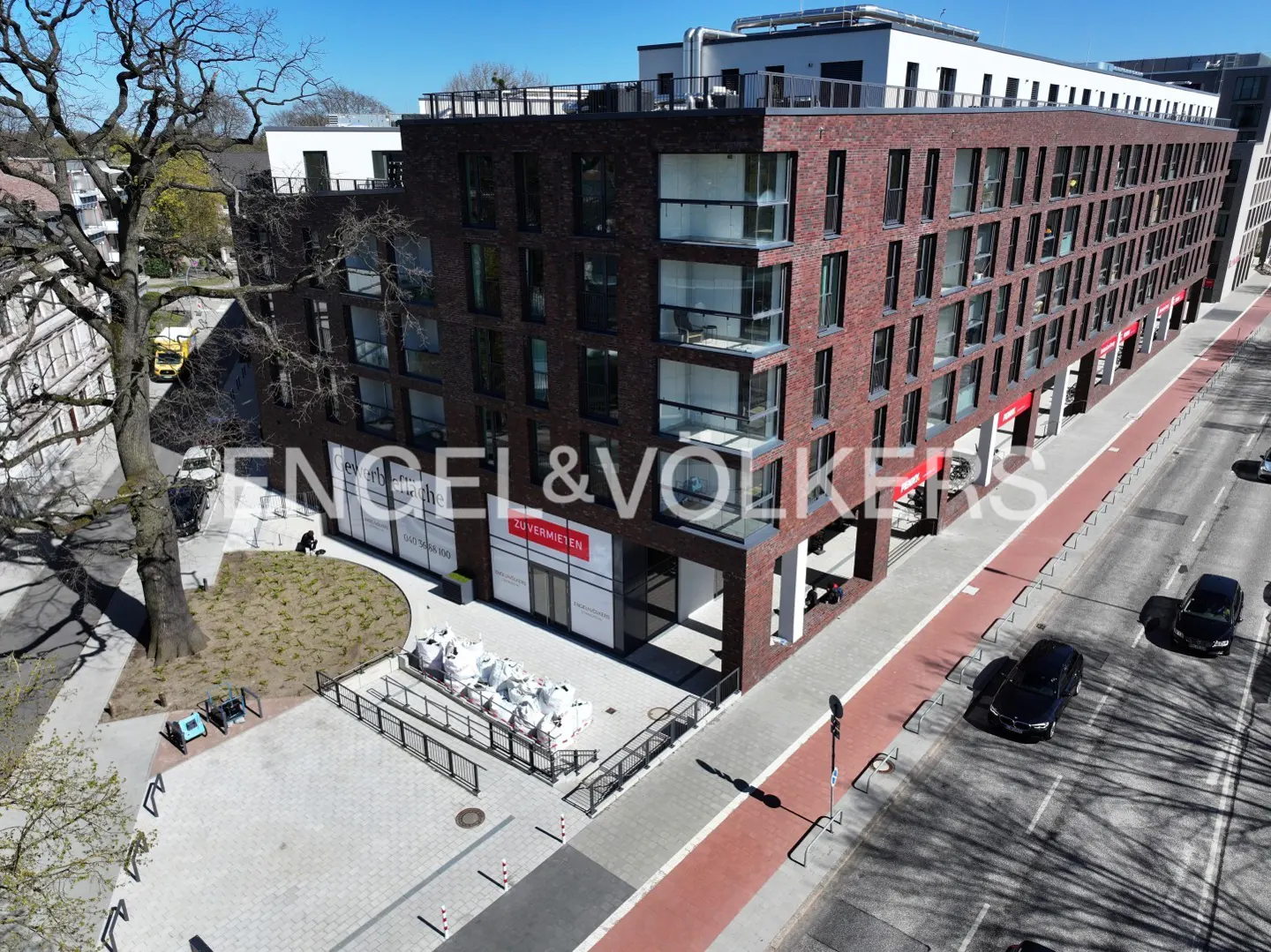 Brick building with Engel & Volkers signage. Bags of material sit outside the entrance. Cars drive on the street.