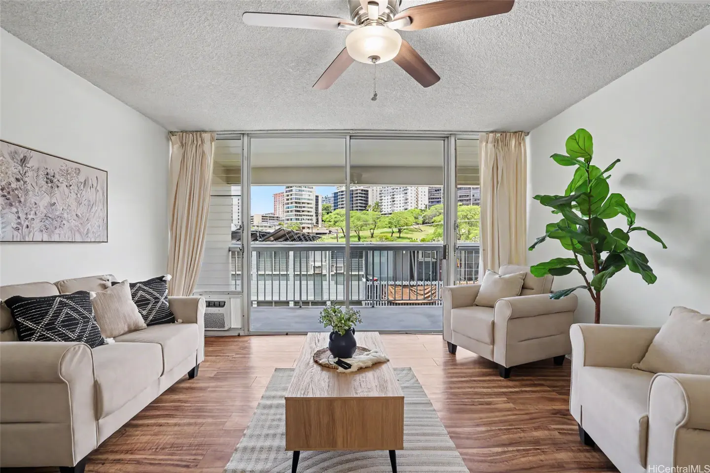 Living room with beige sofa, chairs, wood floors, and a view of a city skyline through sliding glass doors.