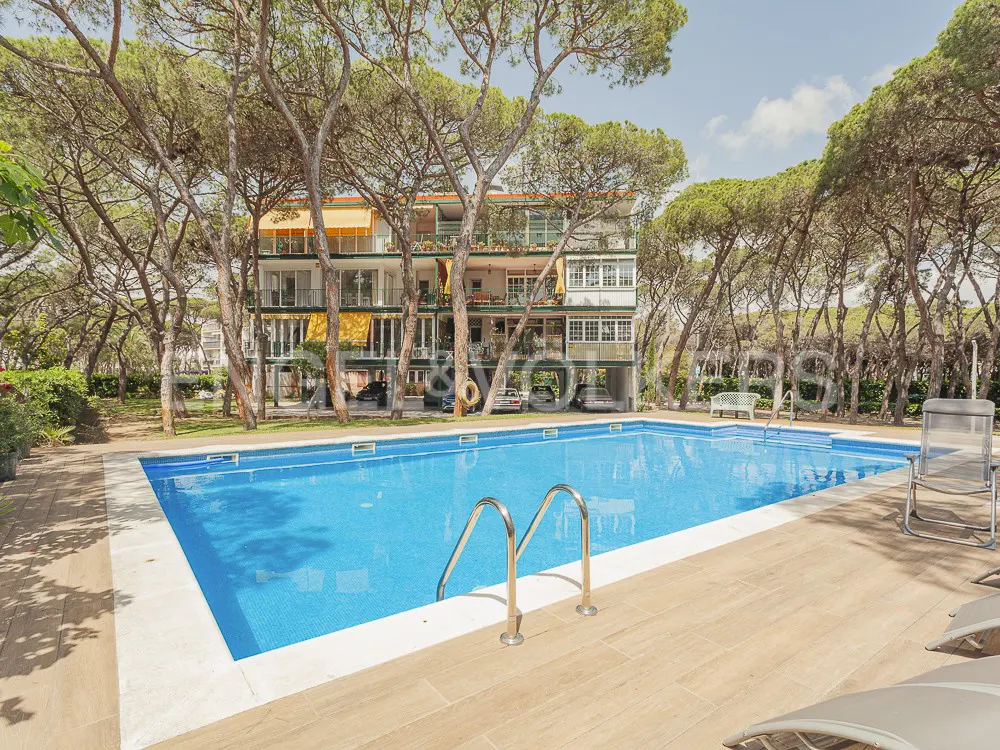 Outdoor pool with metal ladder and tiled deck. A multi-story building is in the background, surrounded by trees.