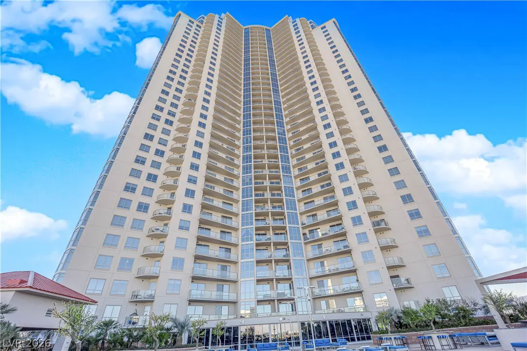 Exterior view of a tall, modern beige condo building with balconies against a blue sky with white clouds.