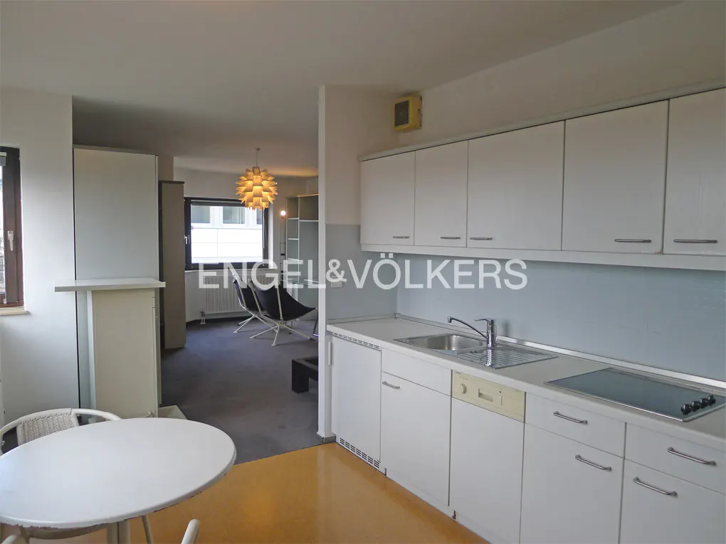 Open-concept apartment with white kitchen cabinets, a sink, and a view into the living room with modern chairs.