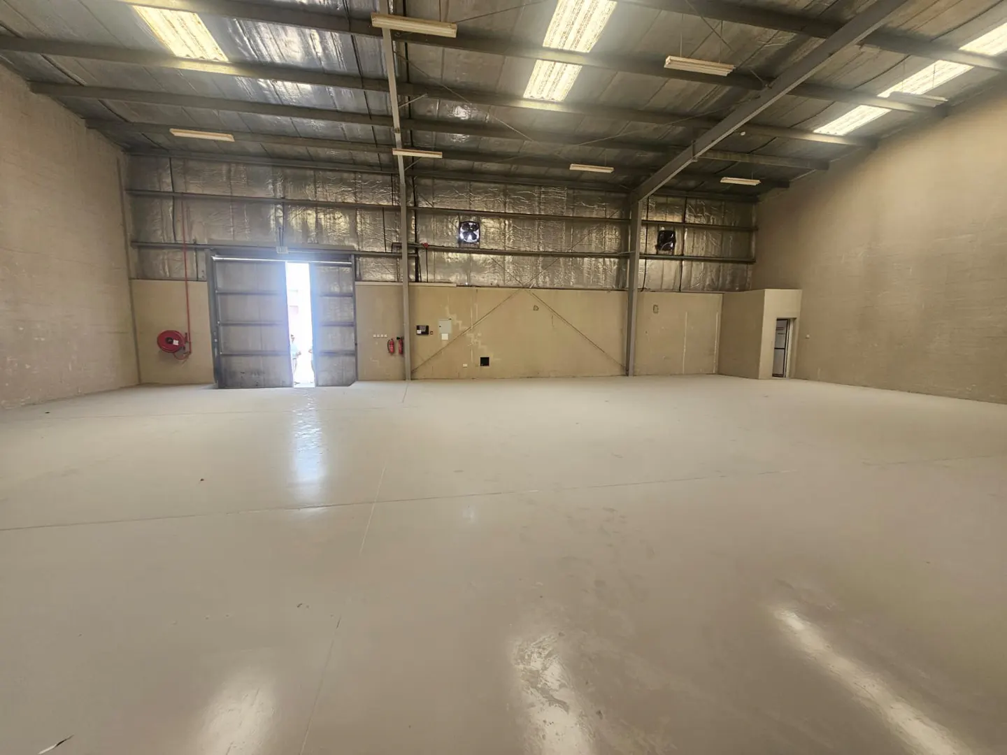 A large, empty warehouse with a concrete floor, metal walls, and an open loading dock door.