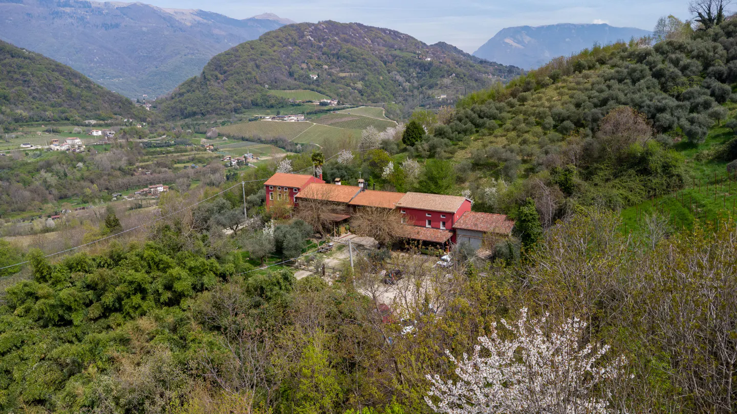 Red house with orange tile roof nestled in green hills, with mountains in the background.