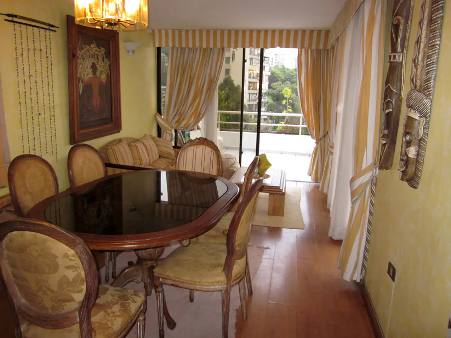 A dining room with a dark wood table, upholstered chairs, and a balcony with yellow and white striped curtains.