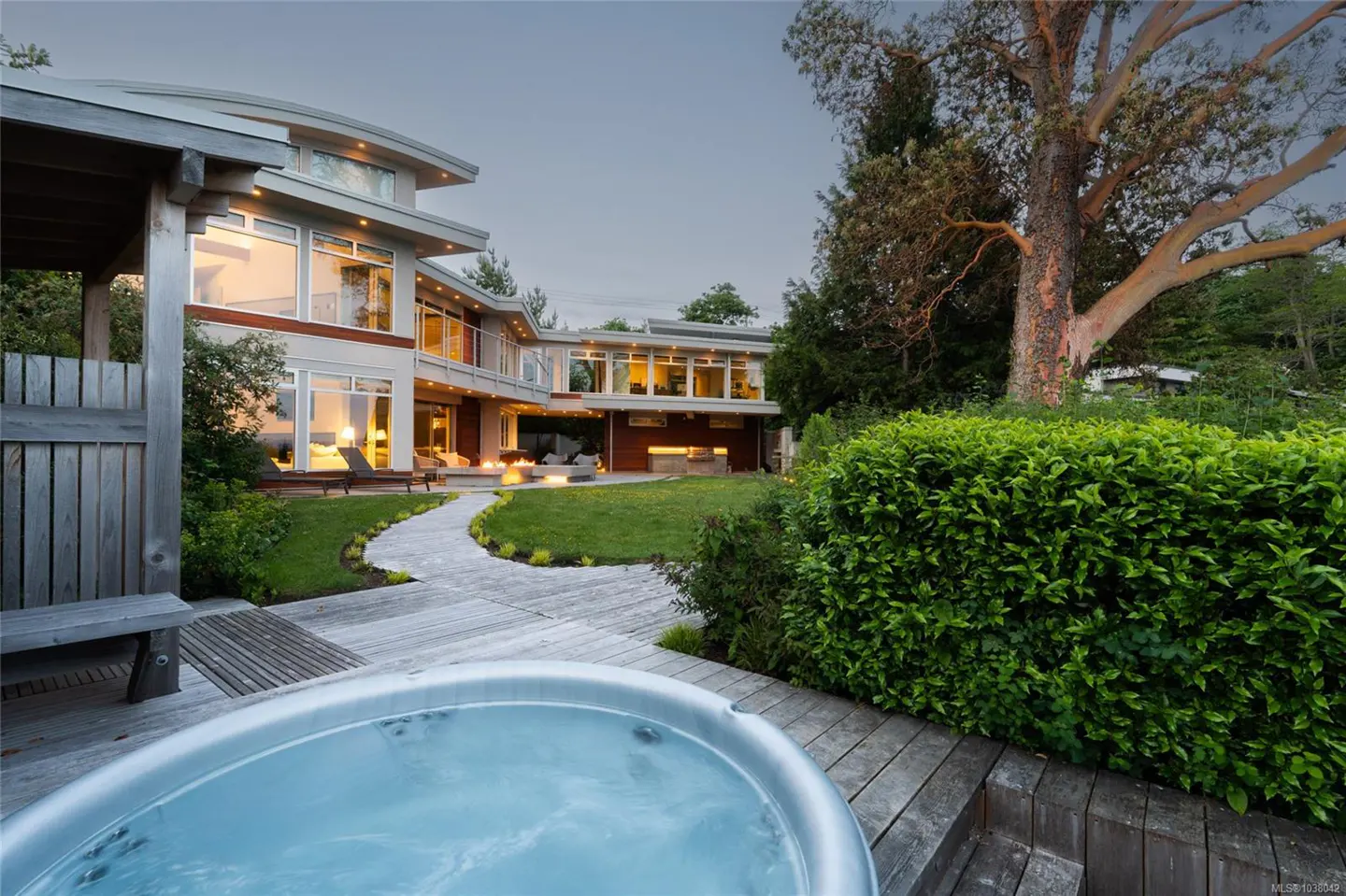 Backyard view of a modern two-story house with a hot tub, lawn, and stone path.