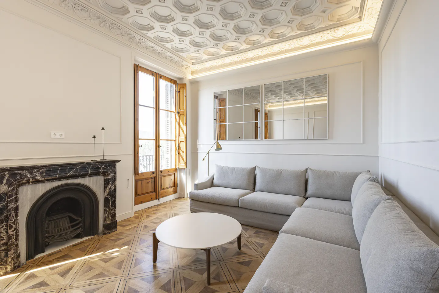 Bright living room with a gray sectional sofa, white table, marble fireplace, and decorative ceiling.