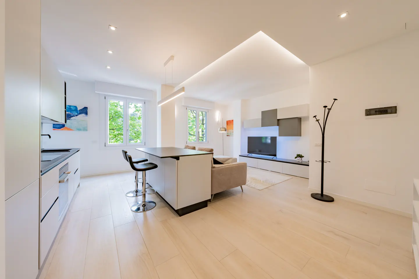 Bright, modern apartment interior with white walls, light wood floors, kitchen island with stools, and living area with TV.
