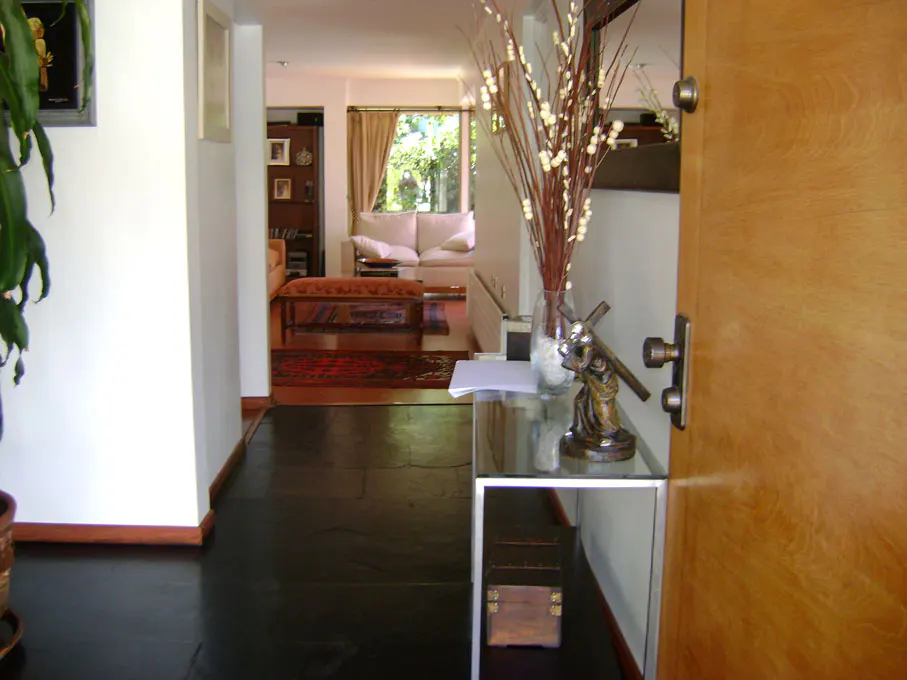 A view from the front door into a home's living room. A glass table with a statue and vase of branches sits near the door. The living room has a white couch and a red rug.