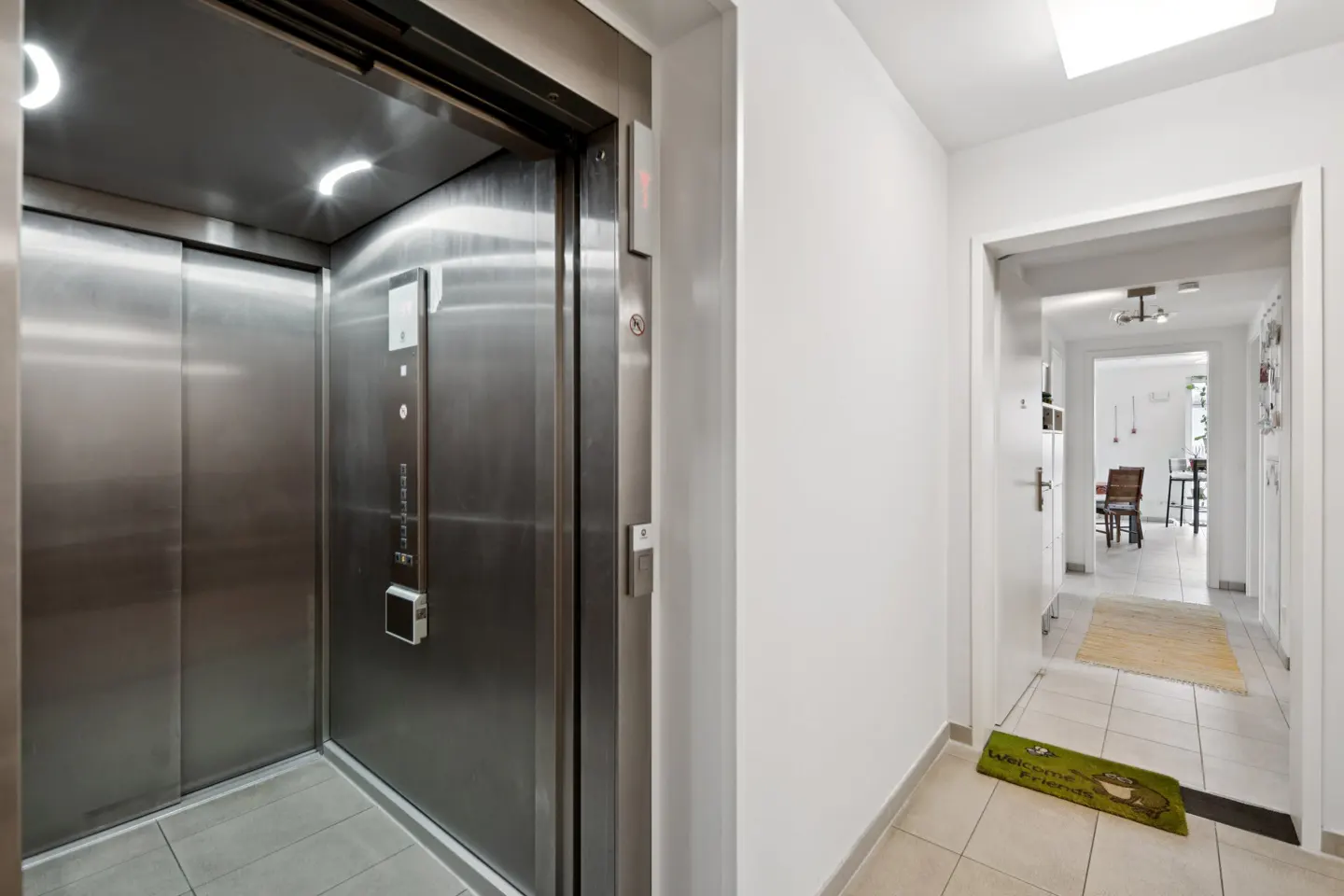 Hallway with an open stainless steel elevator on the left and a doorway leading to a dining area on the right.