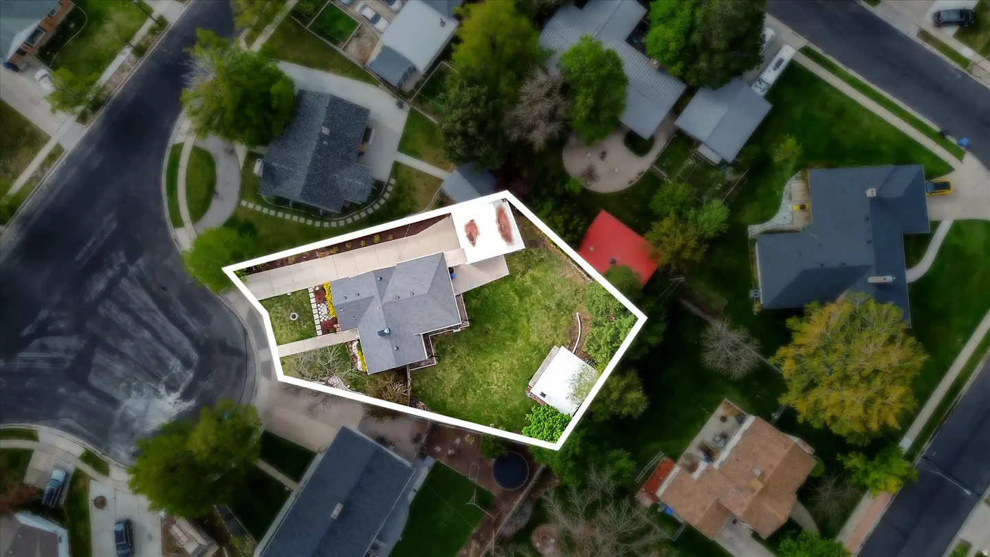 Aerial view of a house with a gray roof, green lawn, and white fence, surrounded by other houses and trees.
