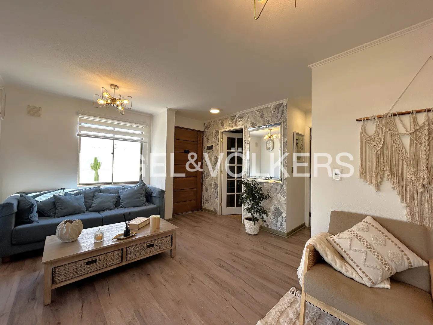 Living room with a blue sofa, wooden coffee table, beige armchair with macramé wall art, and light wood flooring.