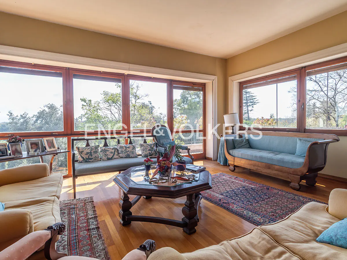 A living room with wood floors, large windows, sofas, and a coffee table. An Engel & Volkers logo is visible in the background.