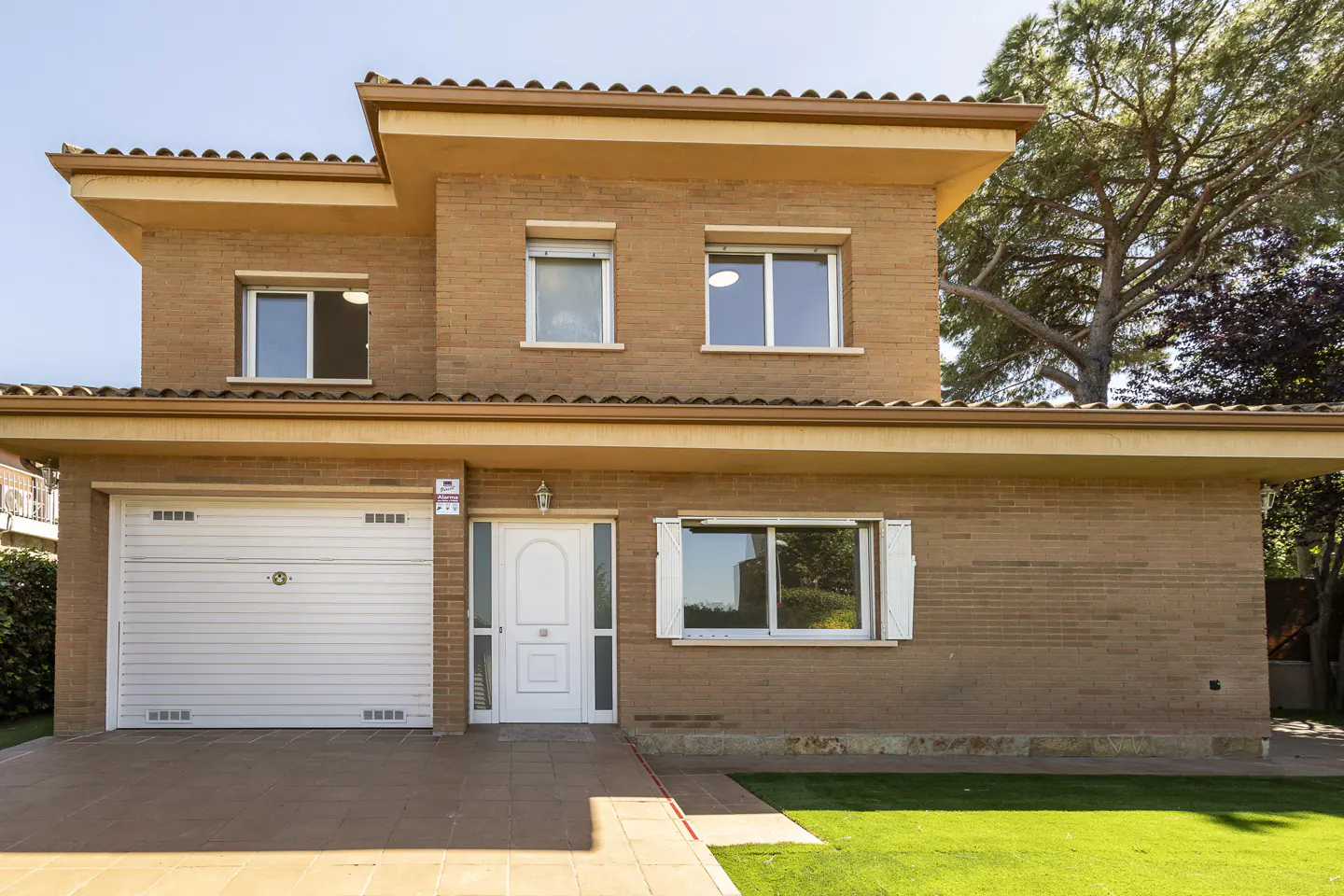 Two-story brick house with white garage door, front door, and window frames. Green lawn in front.