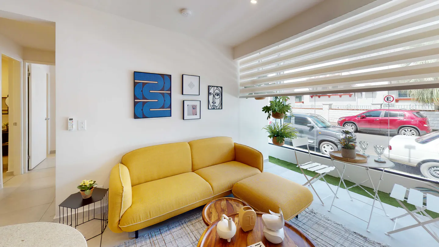 Bright living room with a yellow sofa, wooden tables, and modern art. Large window shows street view with cars.