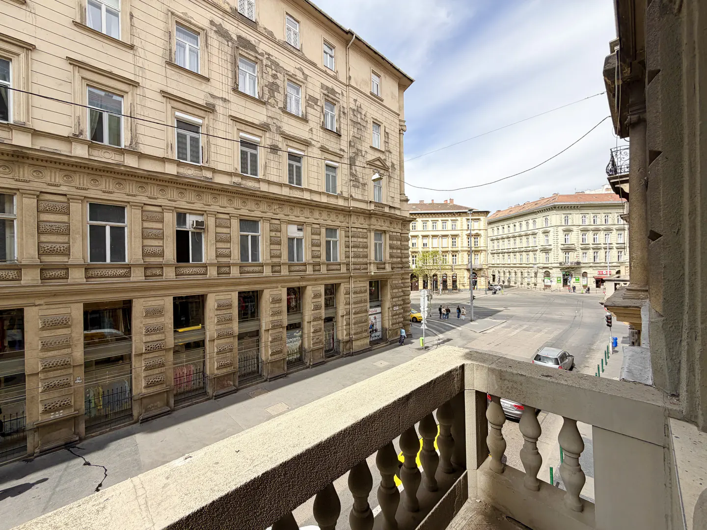 View from a balcony overlooking a European city street with beige buildings and light traffic.