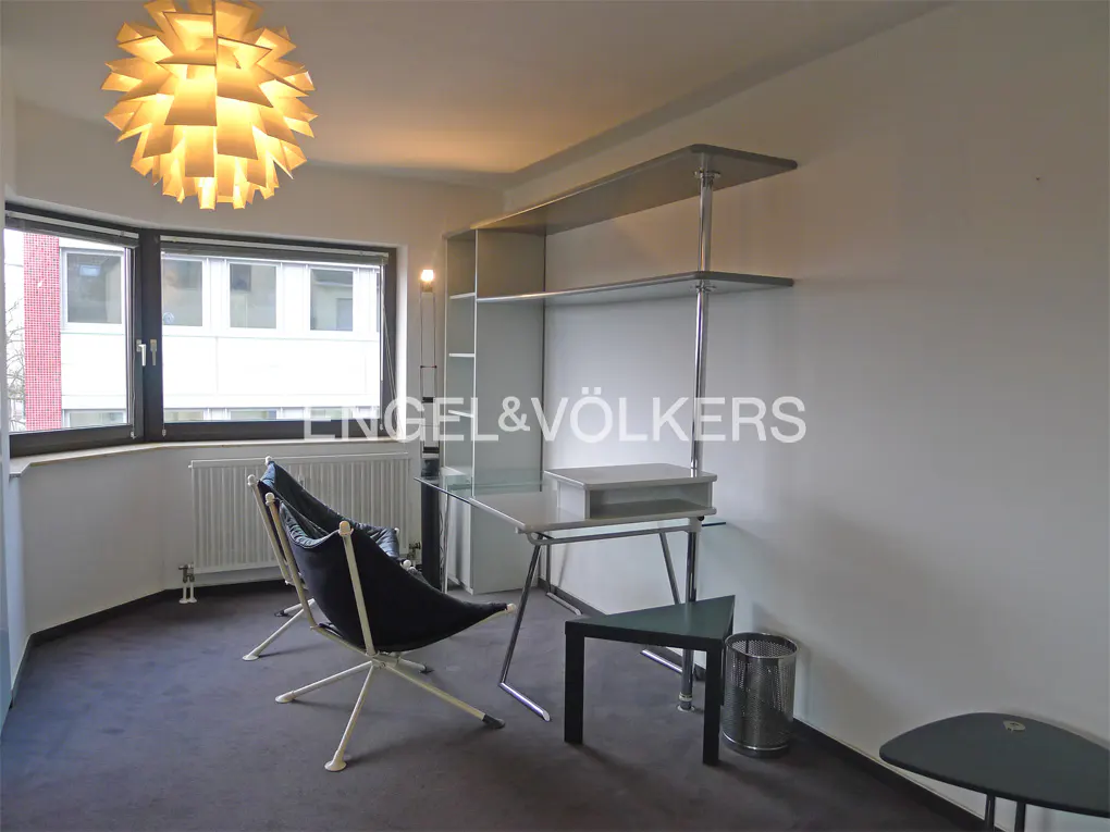 A modern room with a large window, two black chairs, a glass desk, and a unique light fixture.