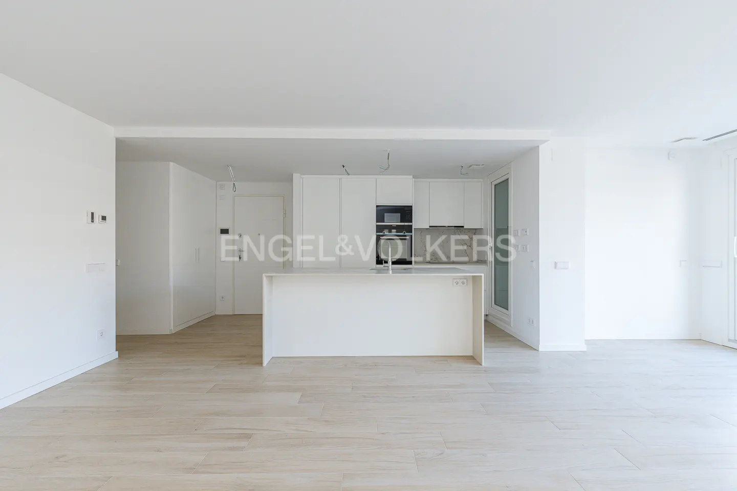A bright, modern kitchen with white cabinets, island, and light wood floors. Engel & Völkers logo visible.