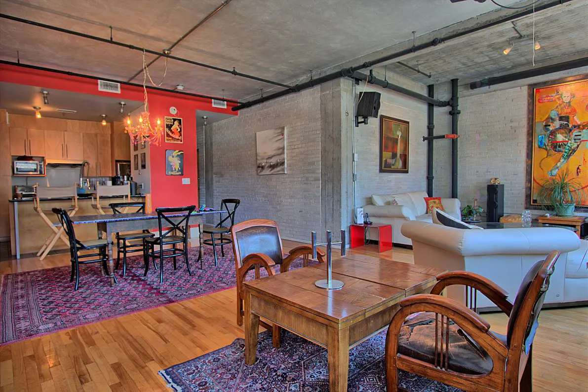 Open-concept loft with exposed brick, hardwood floors, and industrial-style piping. Furnished with modern sofas, tables, and chairs.