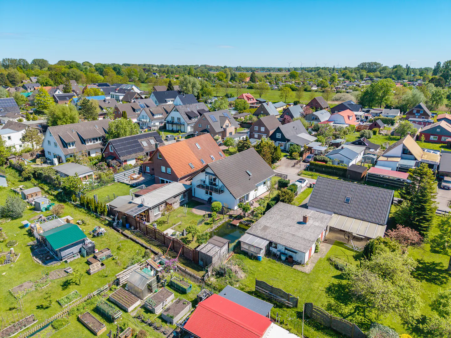 Aerial view of a residential neighborhood with houses, green lawns, trees, and a clear blue sky.