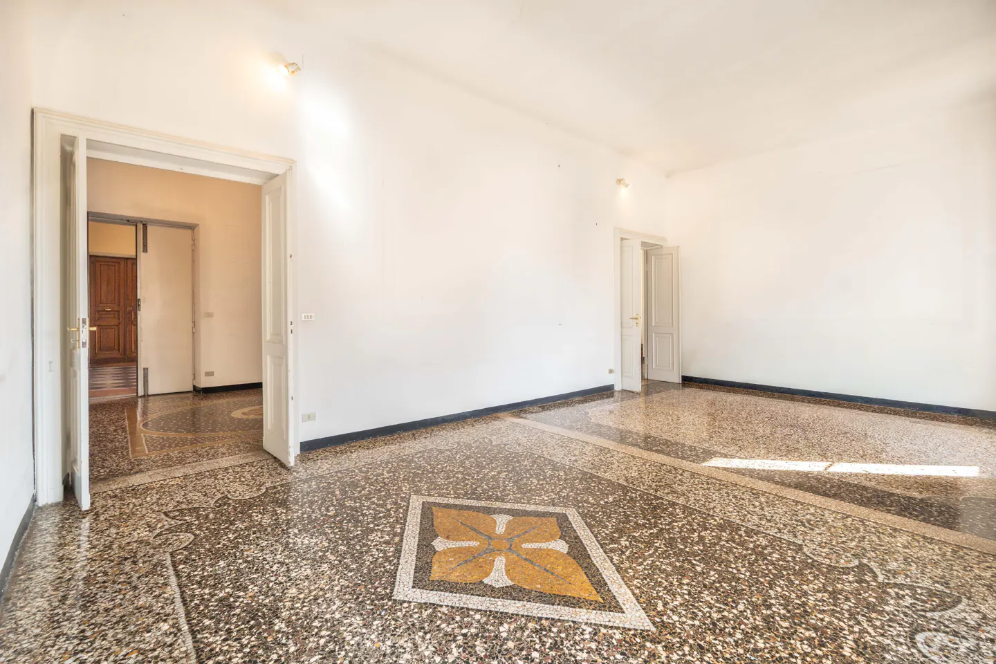 Empty room with white walls, terrazzo floor with a gold flower design, and open doorways.